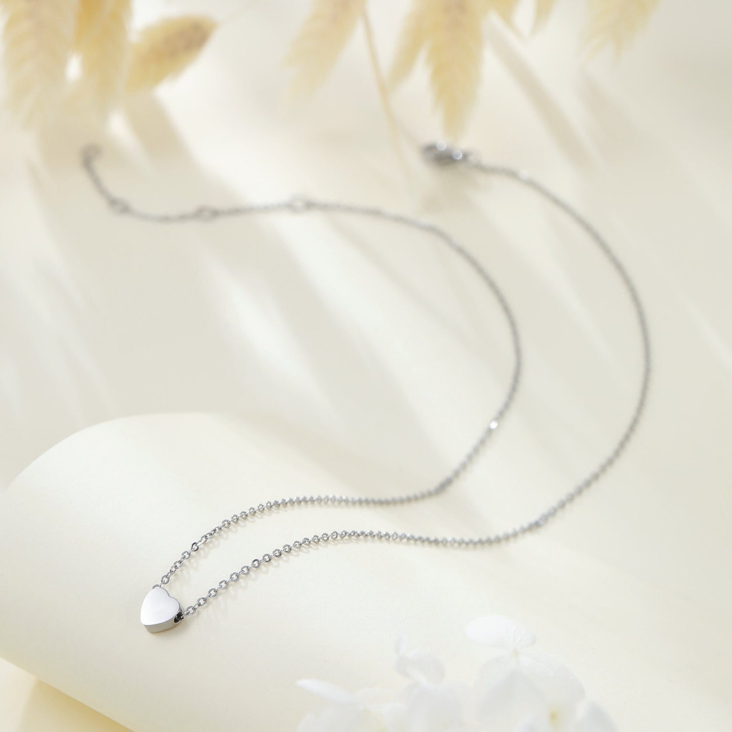 Close up of small polished silver heart charm on a dainty chain.